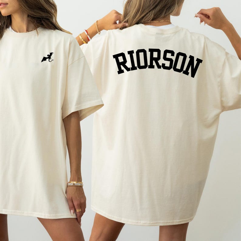 May include: Off-white t-shirt featuring a small black dragon motif on the front and the name "RIORSON" printed in bold black letters on the back. The shirt has short sleeves and a loose fit, suitable for casual wear.