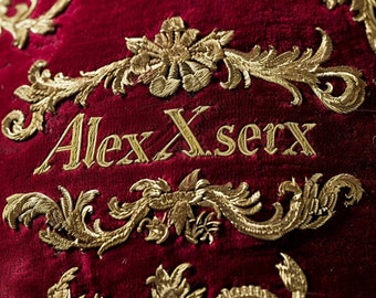 red imperial velvet embroidered with gold ornaments as  handwritten font "AlexXserx"