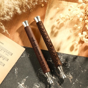 May include: Two wooden pens with silver tops and engraved text. The text on one pen reads "I'll be there for you, no matter what". The pens are on a black and brown surface.