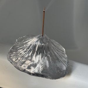 Pode incluir: Um porta-incenso de vidro transparente em forma de montanha com um único pau de incenso a arder e a libertar fumo.