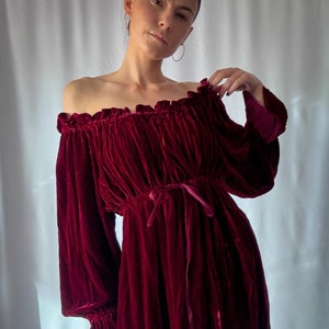 Peut inclure: Une robe en velours bordeaux à épaules dénudées avec des manches longues et un col à volants. La robe a une taille cintrée avec un nœud en ruban.