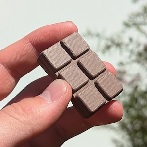 Pode incluir: Uma barra de chocolate marrom com uma superfície texturizada, dividida em nove quadrados.