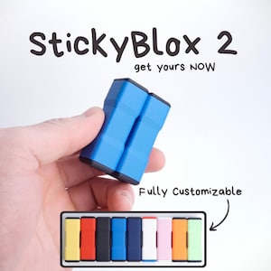 Puede incluir: Un producto azul StickyBlox 2 se sostiene en una mano. El texto "StickyBlox 2" y "get yours NOW" están encima del producto. Una bandeja de StickyBlox coloridos se muestra debajo. También se muestra el texto "Fully Customizable".
