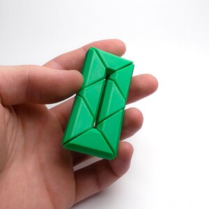 May include: A green triangular puzzle toy with a unique design. The puzzle is made of multiple interlocking pieces that can be manipulated to create different shapes.