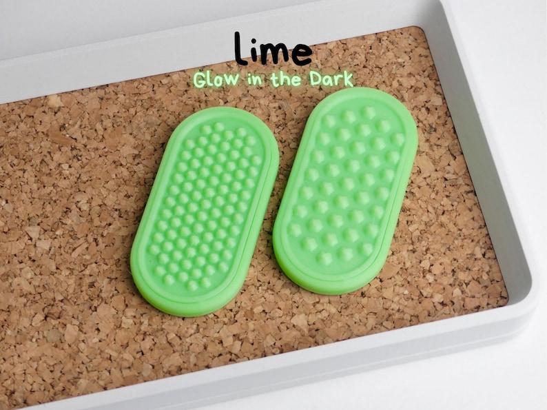 May include: Two lime green, oval-shaped items with textured surfaces, labelled "Lime Glow in the Dark." The items are set on a corkboard within a white tray. The textured surfaces are covered in small, rounded bumps.