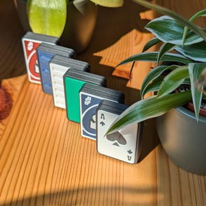 May include: A set of six playing cards with different symbols and colors. The cards are arranged in a row, with the Ace of Spades at the end. The cards are made of a durable material and have a smooth, matte finish.