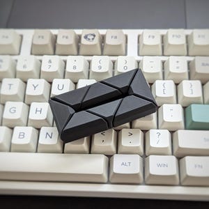 May include: A black plastic keyboard spacer with a geometric design. The spacer is placed on a white keyboard with black keys.