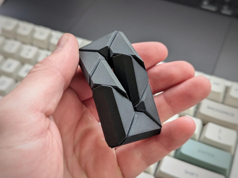 May include: A black, geometric puzzle made of interlocking pieces. The puzzle is in the shape of a rectangle and has a textured surface.