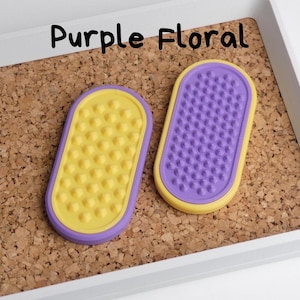 May include: Two oval-shaped, purple and yellow items with textured surfaces are displayed on a corkboard. One is yellow with rounded bumps, the other is purple with small pegs. The text "Purple Floral" is above the items.