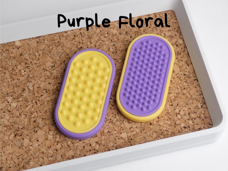 May include: Two oval-shaped, purple and yellow items with textured surfaces are displayed on a corkboard. One is yellow with rounded bumps, the other is purple with small pegs. The text "Purple Floral" is above the items.