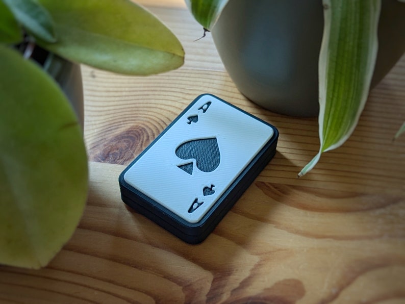 Fidget Slider mit Poker ass Optik. Symbole sind Pik, Kreuz, Herz, Karo. Im Hintergrund ein Schreibtisch.