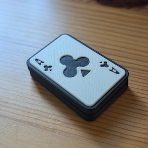 May include: A white playing card with a black ace of clubs symbol. The card is framed in a black border and is slightly angled.