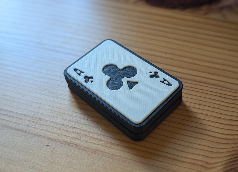 May include: A white playing card with a black ace of clubs symbol. The card is framed in a black border and is slightly angled.