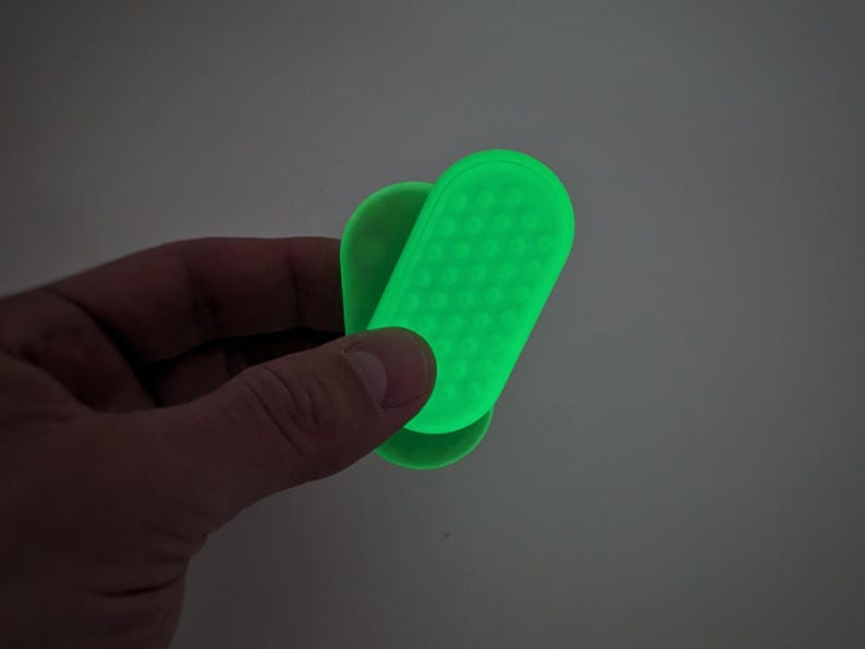 May include: A bright green, handheld device with a textured surface and rounded edges. The device is held in a hand against a neutral background. The device appears to be made of a flexible material.