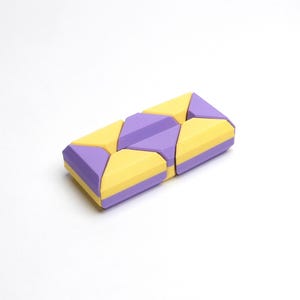 May include: A purple and yellow geometric puzzle toy made of plastic. The puzzle is made up of multiple pieces that can be arranged in different ways.