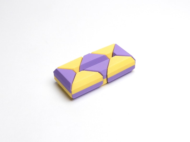 May include: A purple and yellow geometric puzzle toy made of plastic. The puzzle is made up of multiple pieces that can be arranged in different ways.