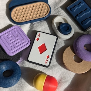 May include: A collection of colorful, textured, and patterned objects, including a playing card with the Ace of Diamonds, a purple donut, a blue donut, a purple square with a pattern, a brown circle with a hole in the center, a blue and white object with a wavy pattern, a yellow and red pill-shaped object, and a white object with a blue circle.