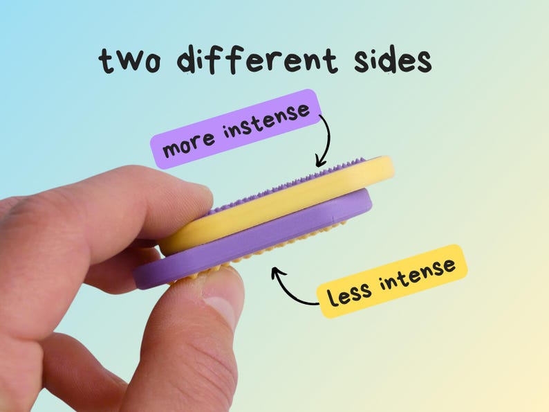 May include: A yellow and purple massage tool with two different sides, held in a hand. The image text reads "two different sides", "more intense", and "less intense". The tool is designed for massage.