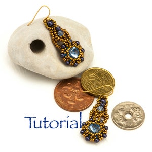 May include: A pair of gold and blue beaded earrings with a teardrop shape. The earrings are hanging from a stone and next to a few coins.