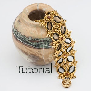 Könnte beinhalten: Ein goldenes und schwarzes Perlenarmband mit floralem Muster. Das Armband hängt an einer Steinvase. Das Wort "Tutorial" steht auf der Oberfläche unter dem Armband.