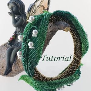 May include: A green and gold beaded bracelet with white pearl accents, shaped like a lily of the valley flower. The bracelet is displayed on a branch with a small fairy figurine sitting on it. The text "Tutorial" is visible in the image.