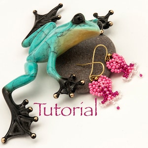 May include: A pair of pink and white beaded earrings shaped like a flower, hanging from gold hooks. The earrings are resting on a stone with a turquoise frog figurine.