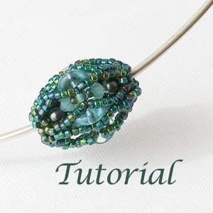 May include: A close-up of a beaded jewellery piece with a turquoise blue and green colour scheme. The beads are arranged in a circular pattern and are strung on a silver wire. The word "Tutorial" is written in green text below the jewellery piece.