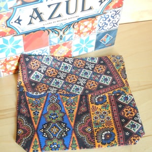 May include: A colorful fabric bag with a paisley pattern in shades of blue, orange, and brown. The bag is folded in half and has a black border.