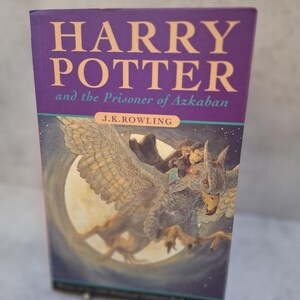 May include: A hardback book titled "HARRY POTTER and the Prisoner of Azkaban" by J.K. Rowling. The cover is purple with gold lettering and an illustration of a creature with a full moon in the background.