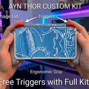Peut inclure: Kit personnalisé Ayn Thor pour console portable avec un couvercle graphique bleu et blanc, des gâchettes rouges et des poignées ergonomiques grises. L'image contient des étiquettes pour le couvercle, les gâchettes et la poignée, ainsi que le texte : Ayn Thor Custom Kit, Free Triggers with Full Kit!