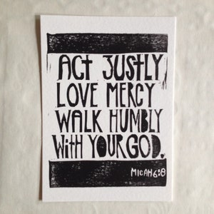 May include: A black and white print on white paper. The text reads "ACT JUSTLY LOVE MERCY WALK HUMBLY WITH YOUR GOD." The text is in a bold, blocky font. The bottom right corner reads "MICAH 6:8".