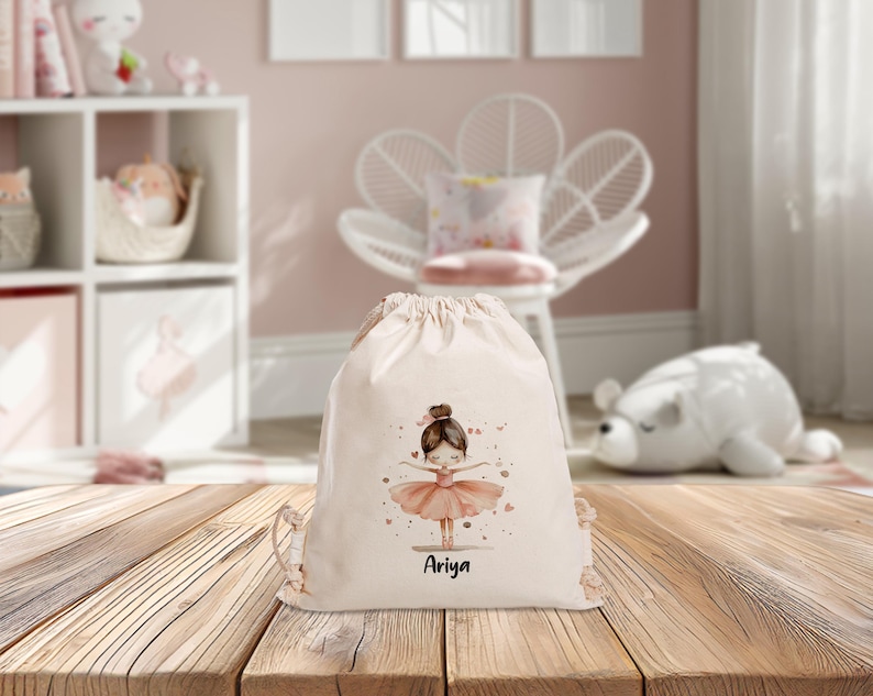 Puede incluir: Una bolsa de cord&oacute;n blanca con una ilustraci&oacute;n de bailarina rosa y el nombre "Ariya" impreso en ella.