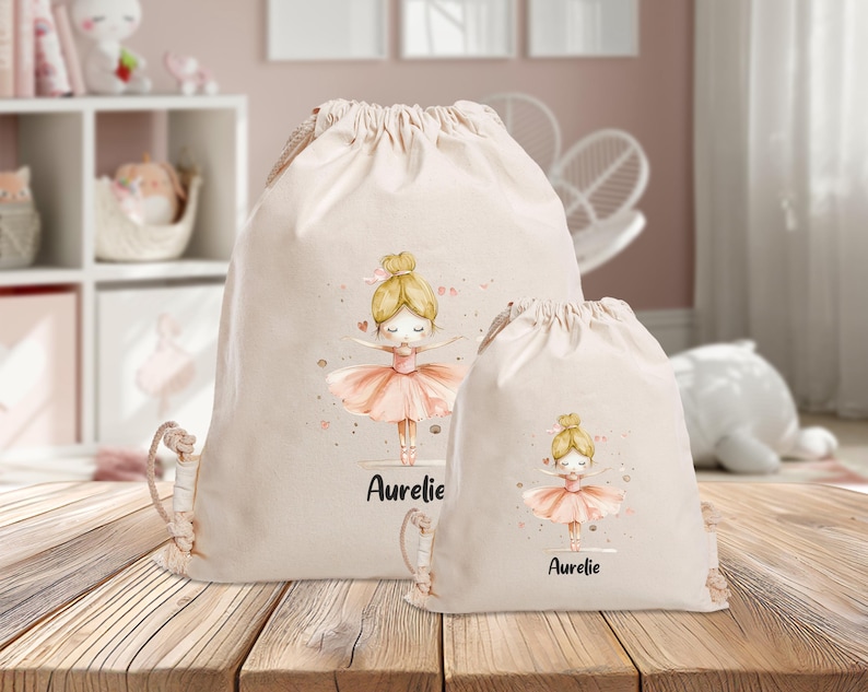 Puede incluir: Dos bolsas de cord&oacute;n beige con una ilustraci&oacute;n de bailarina y el nombre "Aurelie" impreso en cada una. La bailarina lleva un tut&uacute; rosa y tiene el pelo rubio.