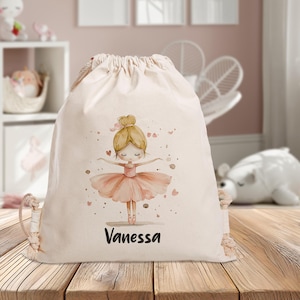 Puede incluir: Una bolsa de cord&oacute;n blanco con una ilustraci&oacute;n de bailarina rosa y el nombre "Vanessa" impreso en la parte delantera.