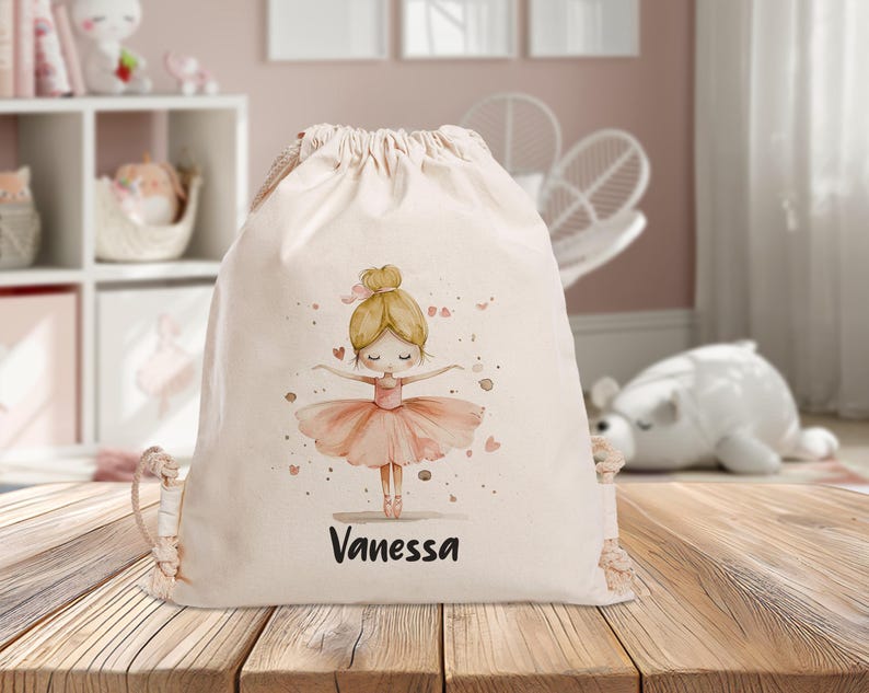 Puede incluir: Una bolsa de cord&oacute;n blanco con una ilustraci&oacute;n de bailarina rosa y el nombre "Vanessa" impreso en la parte delantera.