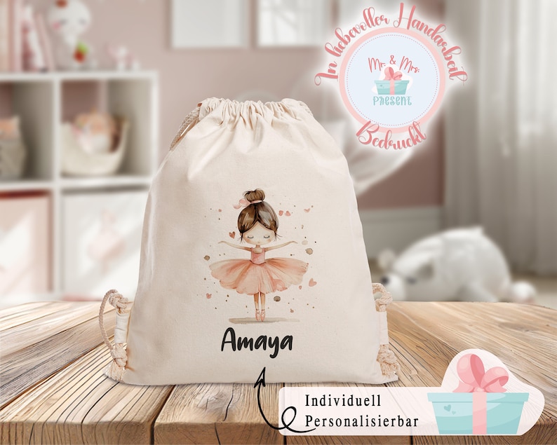 Puede incluir: Una bolsa de cord&oacute;n blanco con una ilustraci&oacute;n de bailarina rosa y el nombre "Amaya" impreso en ella. La bolsa est&aacute; personalizada con el texto "Personalizable individualmente".