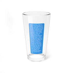 May include: A clear glass with a blue rectangular text overlay. The text includes a message starting with "Good morning, Sienna." The glass is cylindrical with a slightly flared top and a thick base.