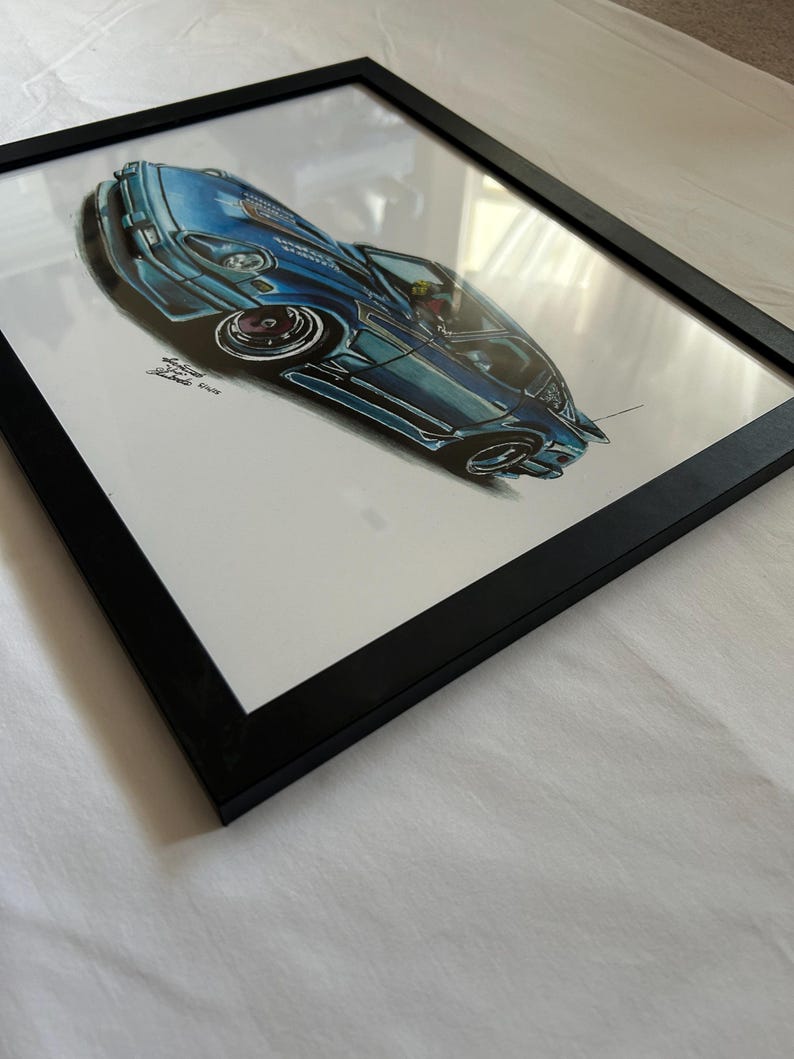 May include: Framed artwork featuring a blue sports car illustration. The car is depicted in a dynamic, angled perspective, with detailed shading and highlights. The artwork is encased in a black frame, adding a modern touch to the automotive art.