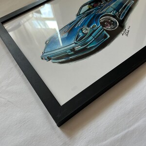 May include: A framed artwork featuring a blue sports car illustration. The car is depicted in a dynamic pose with detailed shading and highlights. The artwork is encased in a black frame, creating a contrast with the white background.