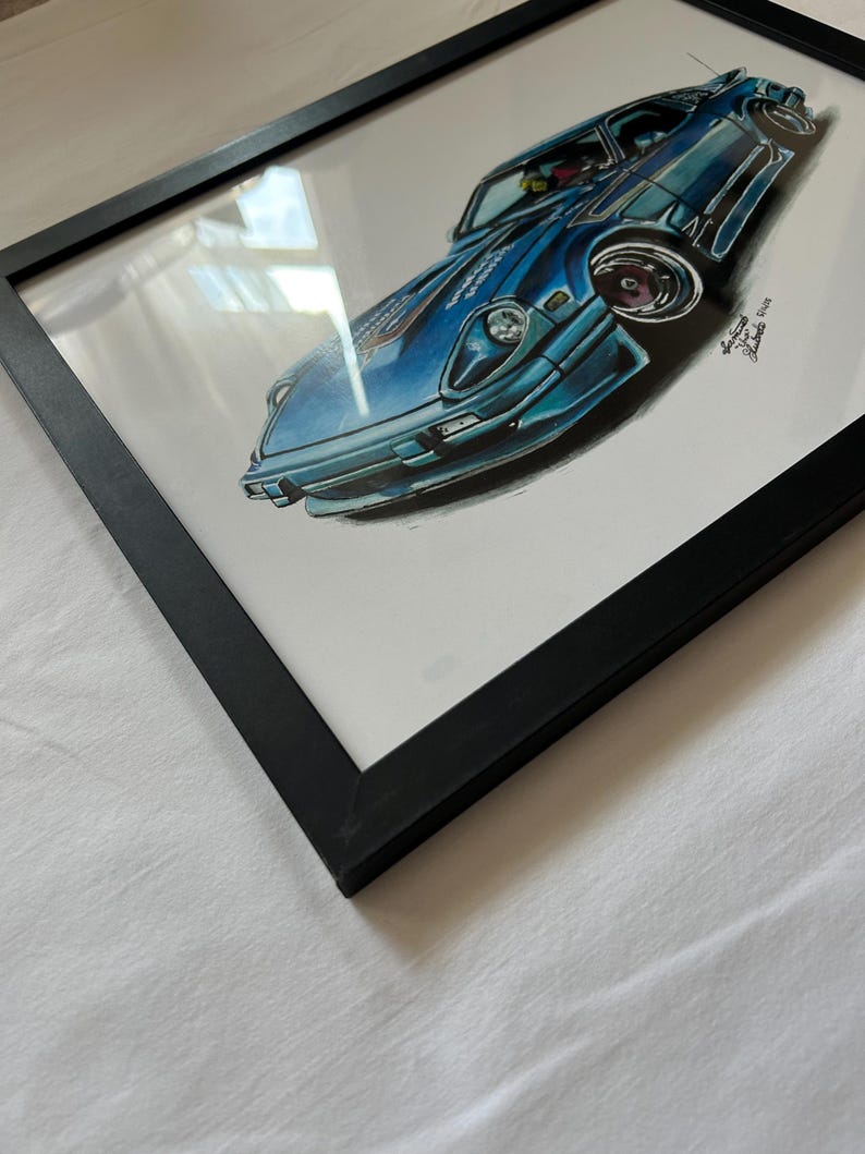 May include: A framed artwork featuring a blue sports car illustration. The car is depicted in a dynamic pose with detailed shading and highlights. The artwork is encased in a black frame, creating a contrast with the white background.