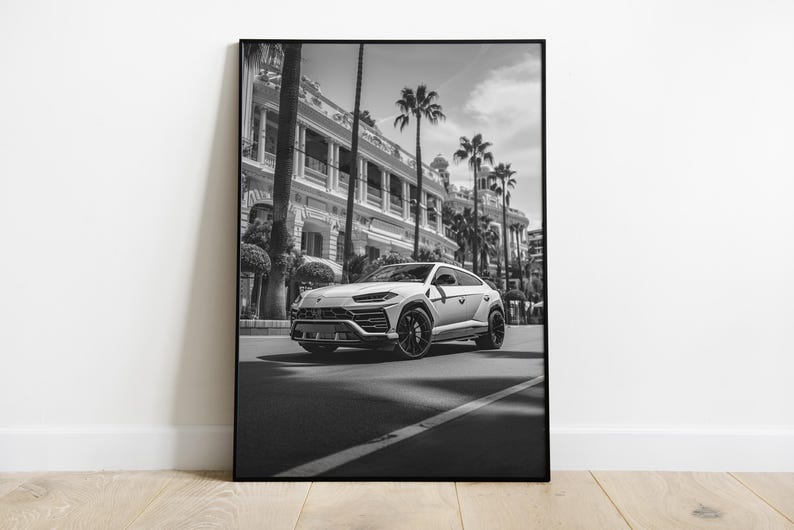 May include: A black and white photograph of a white SUV driving down a street lined with palm trees and a building in the background.