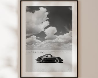 May include: A black and white photograph of a classic car driving on a desert road with a cloudy sky in the background.