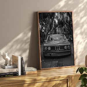 Puede incluir: Impresi&oacute;n fotogr&aacute;fica en blanco y negro de un coche cl&aacute;sico conduciendo por una calle bordeada de &aacute;rboles. El coche es un BMW vintage con una parrilla negra y faros redondos. La foto est&aacute; enmarcada en un marco de madera.