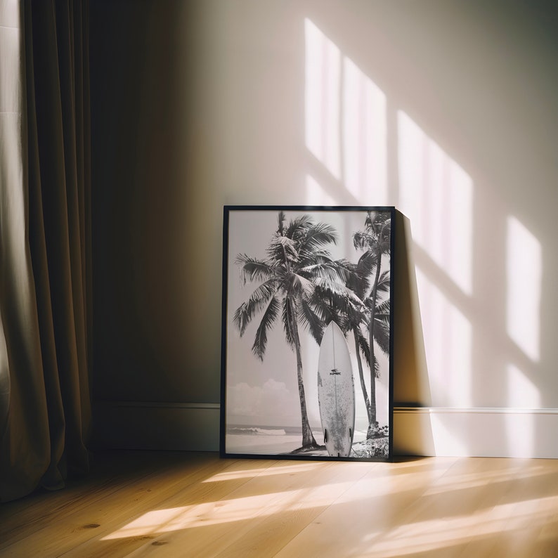 May include: Black and white photograph of palm trees and a surfboard in a framed print. The print is hanging on a white wall.