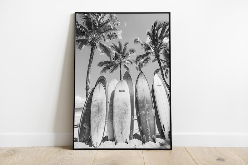 May include: Black and white photograph of five surfboards leaning against palm trees on a beach.