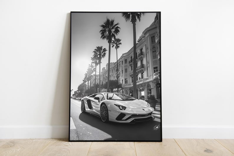 May include: A black and white photograph of a white Lamborghini sports car driving down a street lined with palm trees and buildings. The car is in focus, while the background is slightly blurred.