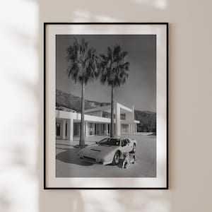 May include: Black and white framed print featuring a luxury sports car parked in front of a modern white house with palm trees. A zebra statue is in front of the car. The image is a photograph.