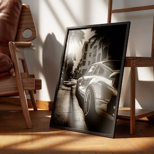 May include: A black and white photograph of a silver Porsche driving down a street lined with palm trees. The photo is framed in a black frame and is leaning against a wooden ladder.