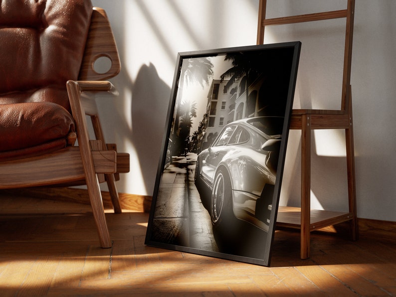 May include: A black and white photograph of a silver Porsche driving down a street lined with palm trees. The photo is framed in a black frame and is leaning against a wooden ladder.