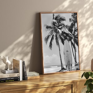 May include: Black and white photograph of palm trees and a surfboard on a beach. The image is framed in a wooden frame.